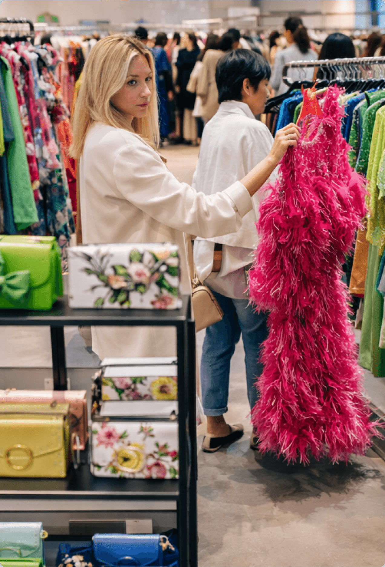 Shopper browsing a vibrant clothing rack at a 260 Sample Sale in-store event, holding a hot pink feathered gown