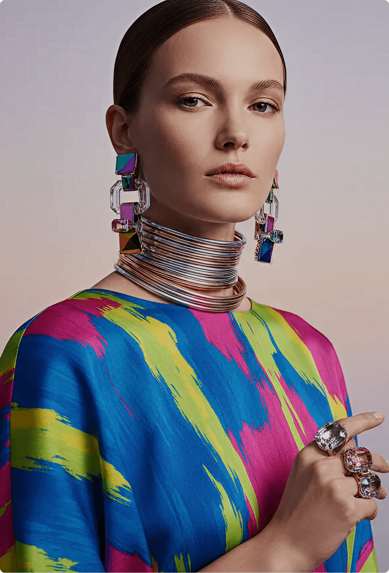 Model wearing a bold multicolor abstract dress with oversized crystal earrings and layered silver neck rings
