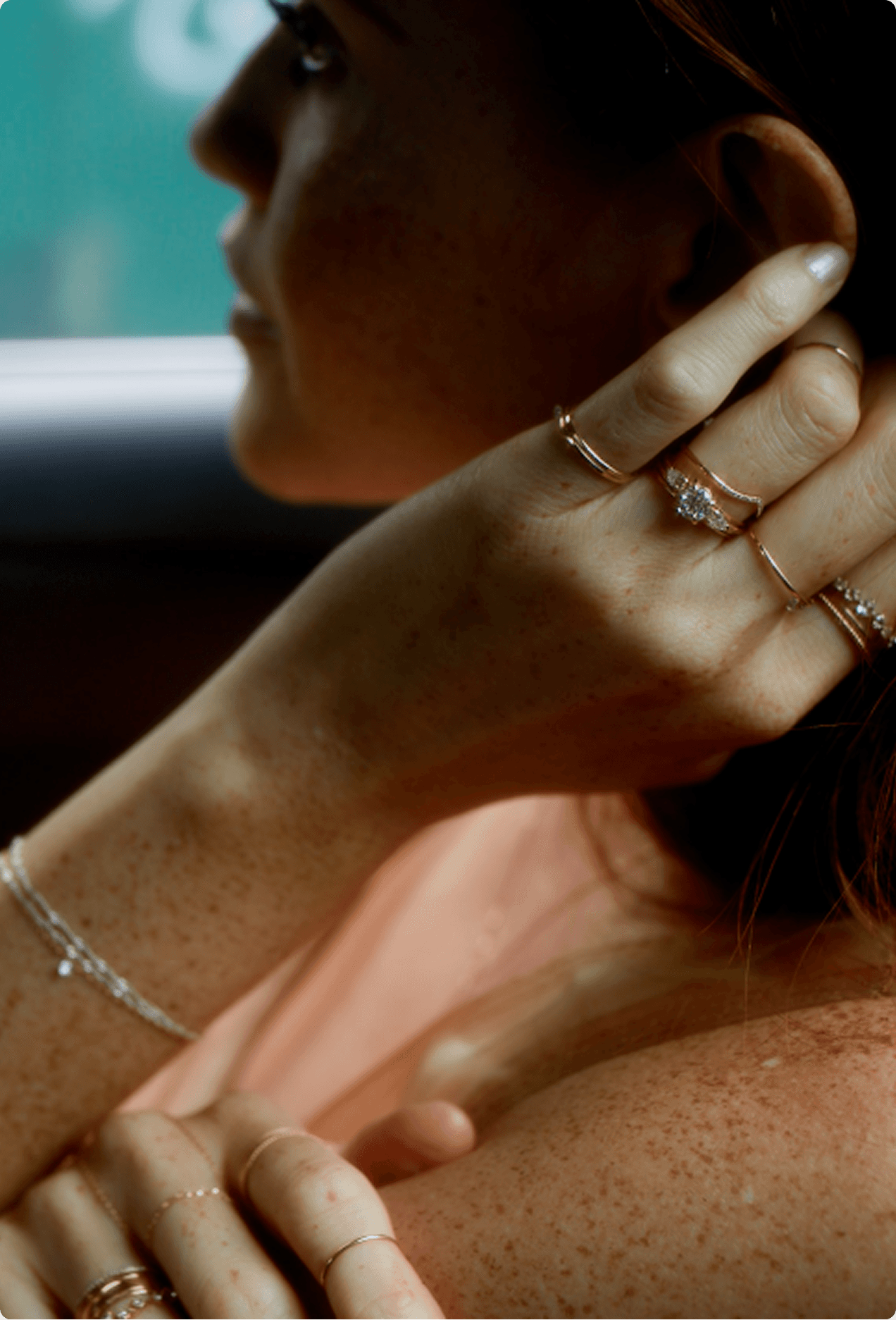 Close-up of a woman's hand and neck with stacked Catbird NYC gold rings and a delicate chain necklace in warm light