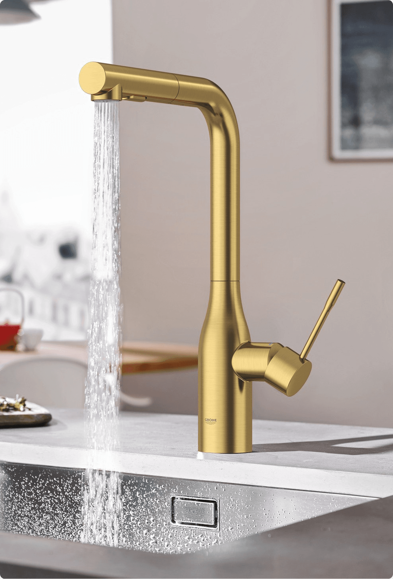 GROHE brushed gold kitchen faucet with pull-down spray running water over a stainless steel sink