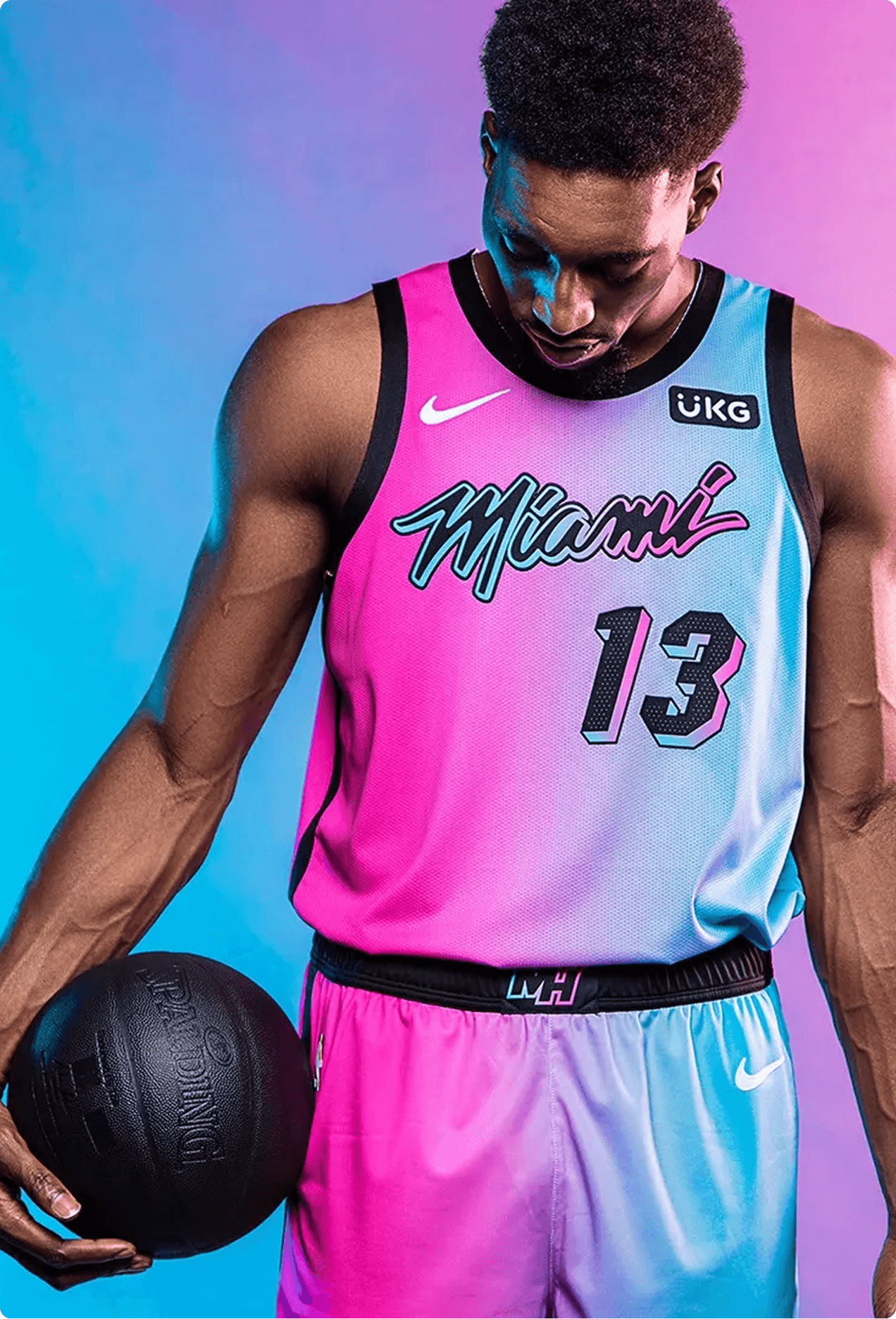 Miami Heat player Bam Adebayo wearing the Vice Jersey, pink and blue gradient, holding a basketball against a studio backdrop