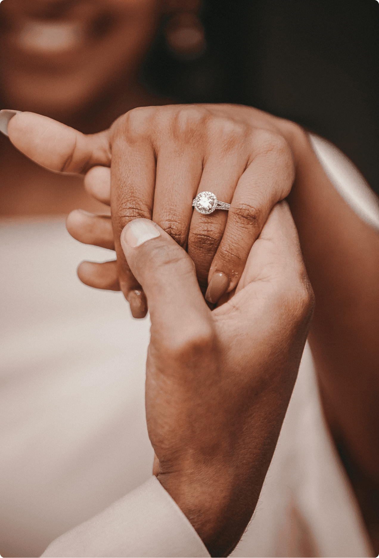 Close-up of a couple holding hands, woman wearing a round halo diamond engagement ring