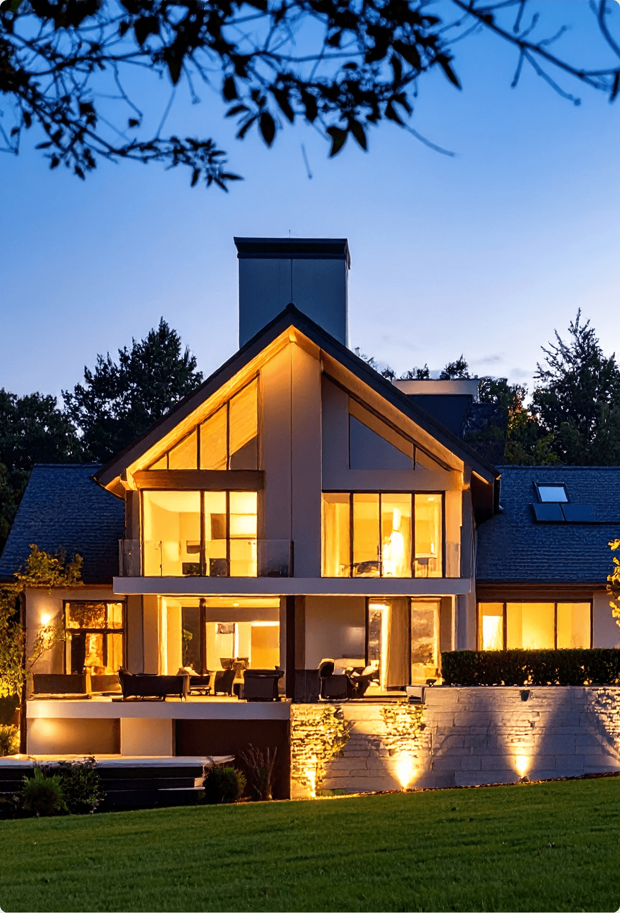 Modern home exterior at dusk with warm SATCO lighting illuminating the facade, patio, and landscaping